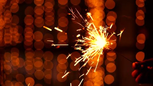 Hand holding or burning a sparkler or cracker in a decorative festive background with copy space. A sparkler is sparkling by a person on Diwali, celebrating New year, Birthday.